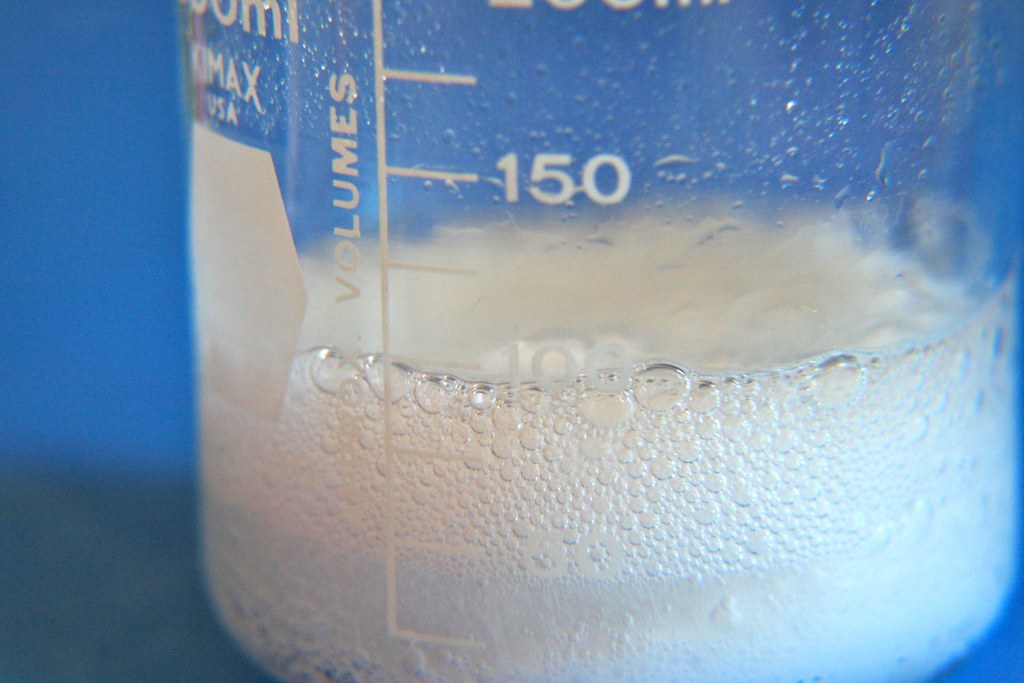 Bubbling, frothing white fluid in a flask against a blue background.