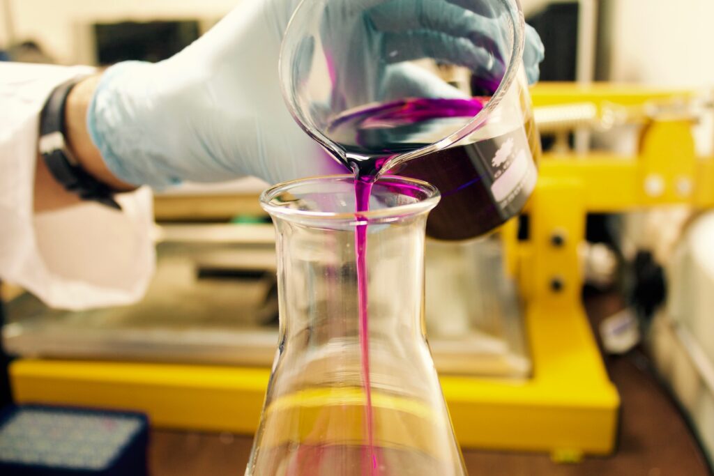 Blue gloved hand pouring thick purple liquid into a flask
